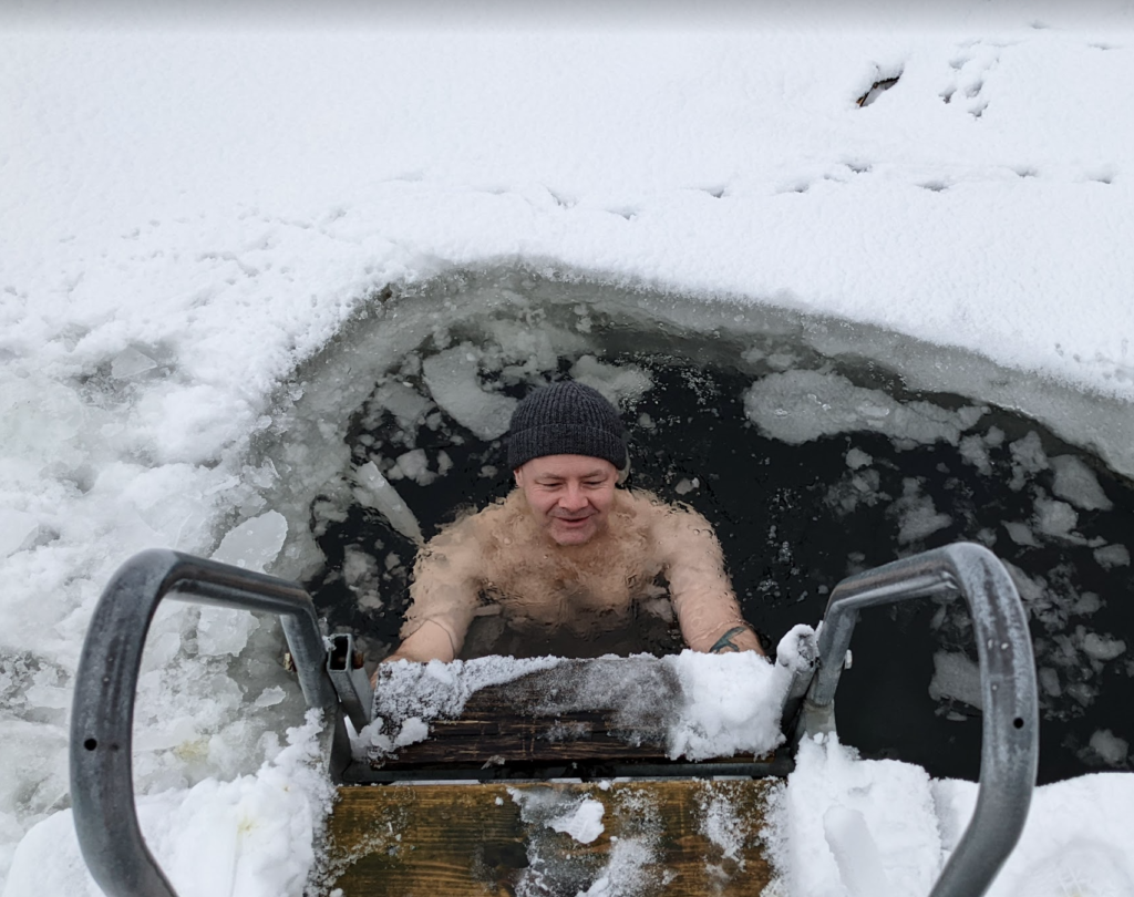 SK in taking a dip hole in the ice wearing a woolly hat.